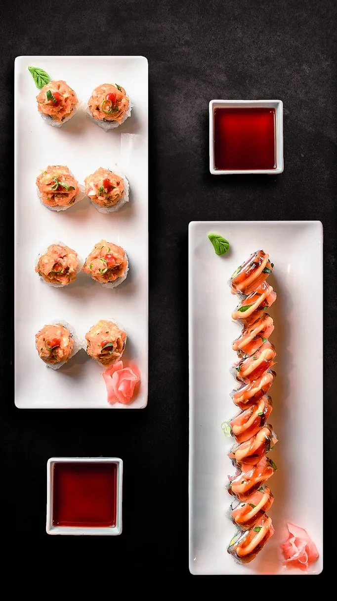 Two sushi platters with dipping sauces on a dark table